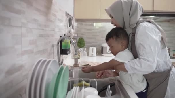 Мусульманская мать моет сына рукой в кухонной раковине — стоковое видео