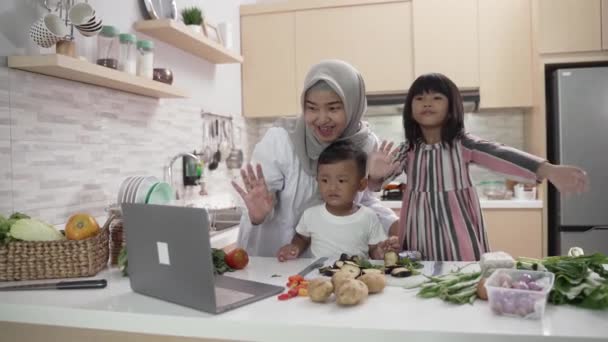 Mãe muçulmana assistindo cozinhar vídeo no laptop e fazer o jantar com seus dois filhos — Vídeo de Stock