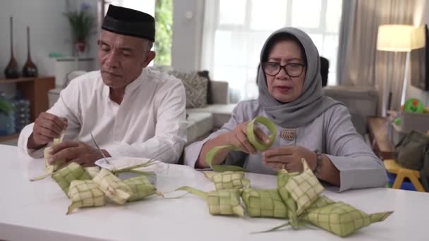 Pareja musulmana e hija haciendo ketupat para eid fitr mubarak celebración en casa — Vídeos de Stock