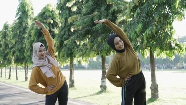 Two Muslim girls in headscarves stretch their muscles by raising their hands to exercise outside the room — Stock Video