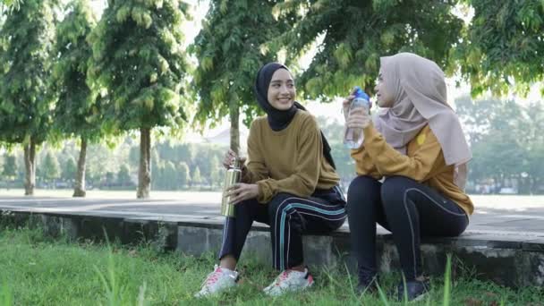 Mosolygós két muszlim tizenéves lány ivóvíz használata üveg sport után együtt délután — Stock videók