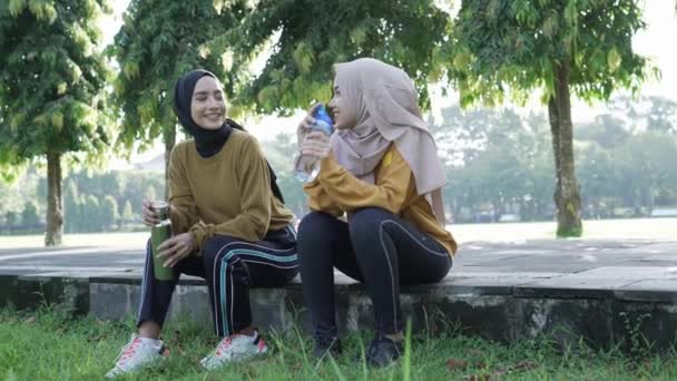 Souriant deux adolescentes musulmanes boire de l'eau en utilisant des bouteilles après le sport ensemble dans l'après-midi — Video