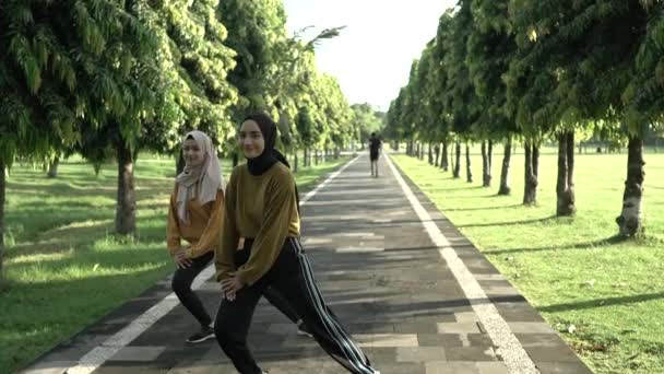 Dos chicas musulmanas veladas estiran sus manos antes de trotar y practicar deportes al aire libre — Vídeo de stock