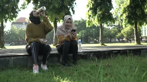 Sonriendo a dos adolescentes musulmanas bebiendo agua usando botellas después de deportes juntos en la tarde — Vídeo de stock