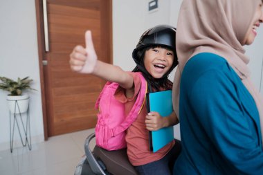 Müslüman anne sabah kızını motosikletle okula götürüyor.