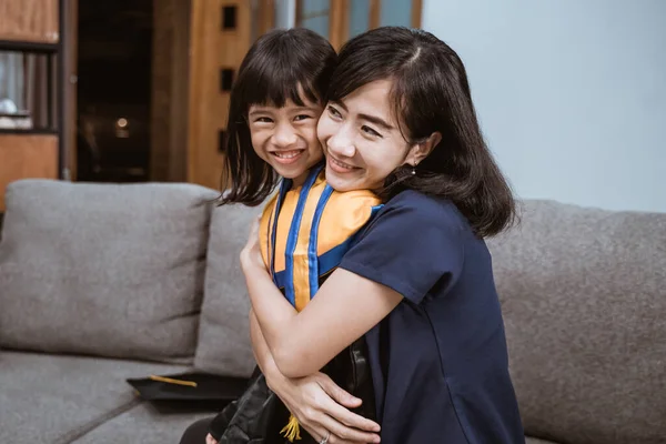 Горда азіатська мати обіймає свою дочку під час дня випуску початкової школи — стокове фото