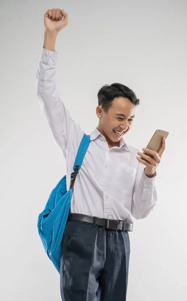 En pojke klädd i en junior high school uniform tittar på en telefon med upphöjd hand en upphetsad gest — Stockfoto