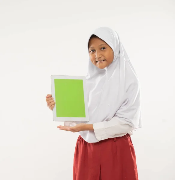 Uma menina vestindo um uniforme de escola primária com capuz fica segurando um tablet digital e mostrando a tela do tablet para a câmera — Fotografia de Stock