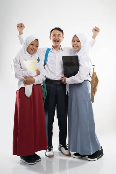 Three smiling teenagers wearing school uniforms with a backpack, a book, and a laptop computer — Stock Photo, Image