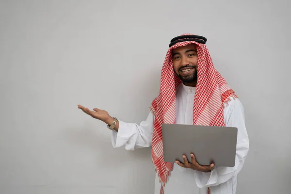 Un turbante arabo sorridente mentre tiene in mano un computer portatile e dall'altra parte presenta qualcosa — Foto Stock