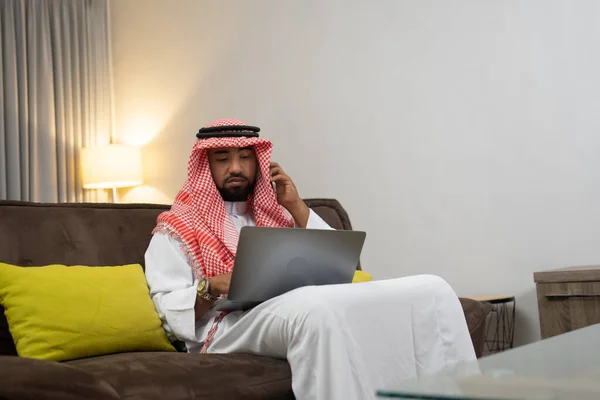 Arabski biznesmen noszący turban używa telefonu komórkowego do wykonywania połączeń i korzysta z laptopa — Zdjęcie stockowe