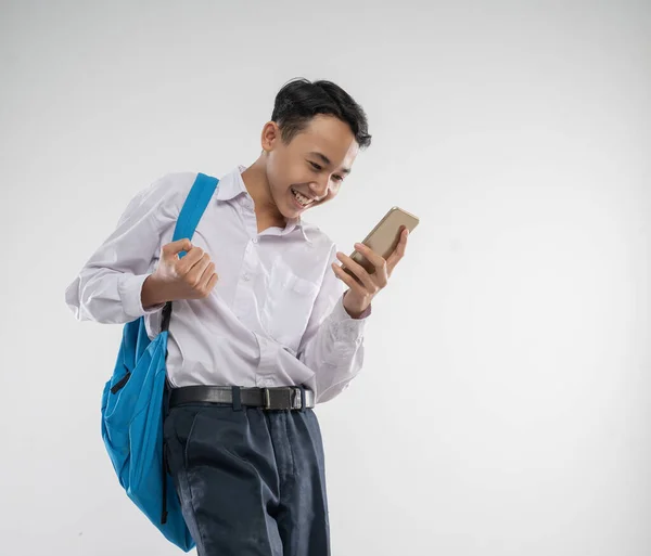 A boy wearing a junior high school uniform looking at a cellphone with an excited gesture with a backpack — Stock Photo, Image