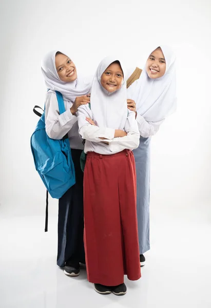 Tiga gadis tersenyum mengenakan kerudung dalam seragam sekolah melihat ke kamera dengan tas sekolah — Stok Foto