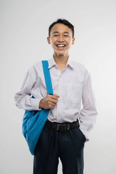 Un niño sonriente vistiendo un uniforme escolar y llevando una mochila con las manos embolsadas —  Fotos de Stock