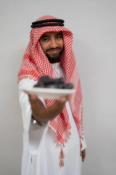 En arabian i en turban leenden medan du bär och erbjuder en tallrik med datum till kameran — Stockfoto