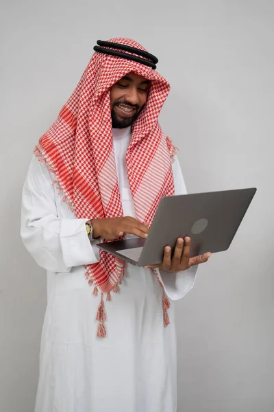 Arabski w turbanie uśmiechnięty podczas korzystania z laptopa — Zdjęcie stockowe