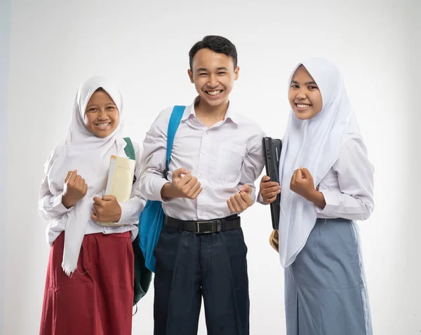 Tre tenåringer i skoleuniform smilte med opphisset håndbevegelse når de bar ryggsekk og en bok – stockfoto