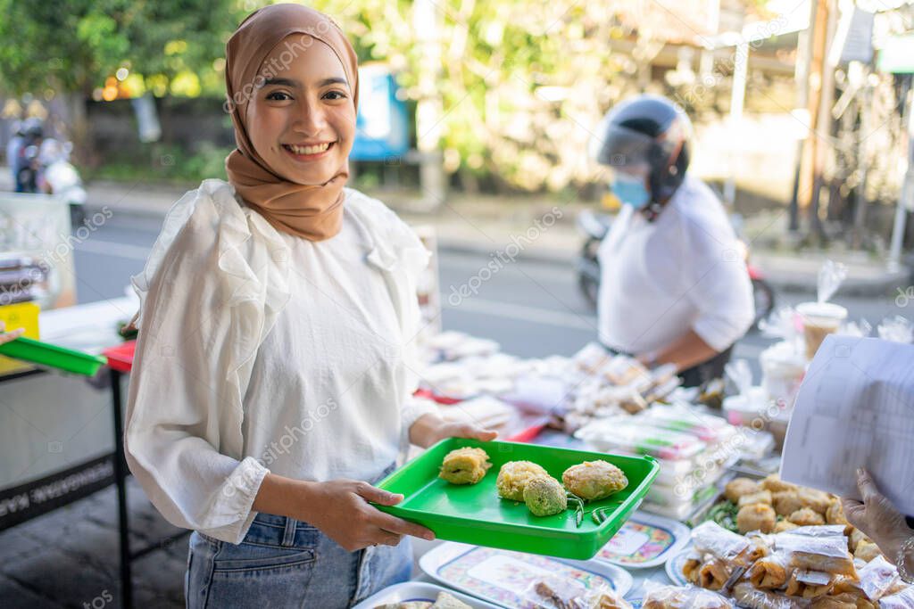 smiling a beautiful girl in a veil hold plastic tray selling various kinds of fried foods