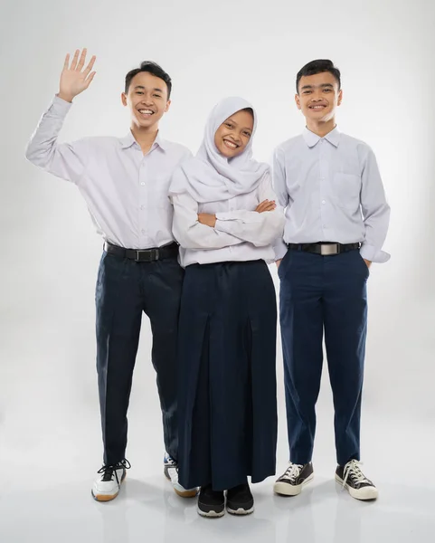Três adolescentes de uniforme do ensino médio ficam sorrindo para a câmera enquanto cumprimentam com um gesto de mão — Fotografia de Stock