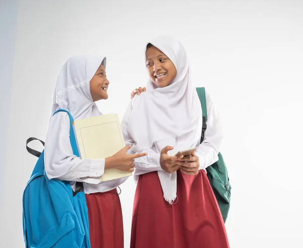 Duas meninas veladas vestindo uniformes do ensino fundamental conversando com mochilas e um livro — Fotografia de Stock