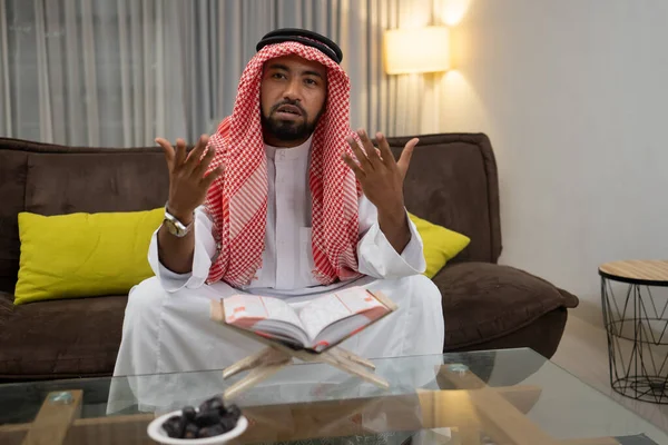 En arabisk ung man läser Koranen med uttryck av sina händer tittar upp — Stockfoto
