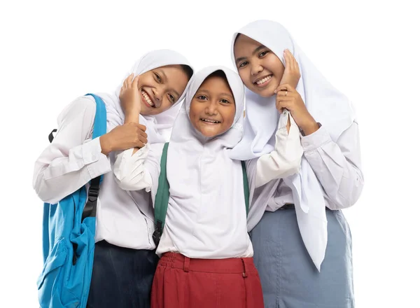 Tiga orang asia berkerudung dengan seragam sekolah berdiri tersenyum dengan sikap kasih sayang satu sama lain sambil membawa ransel — Stok Foto