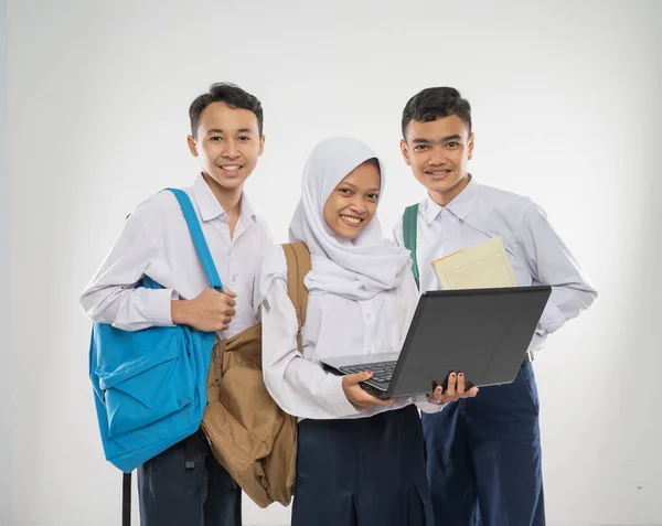 Group of teenage wearing school uniforms using a laptop computer together while carrying a backpack and a book — Stock Photo, Image