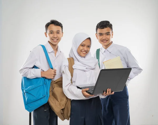 Skupina teenagerů ve školních uniformách, kteří společně používají notebook při nošení batohu a knihy — Stock fotografie