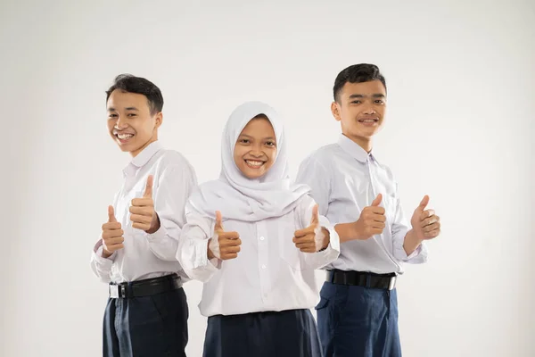 Drie lachende tieners dragen junior middelbare school uniformen staan met duimen omhoog — Stockfoto