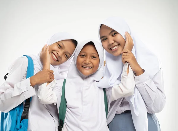 Tiga gadis berkerudung mengenakan seragam sekolah berdiri tersenyum dengan sikap kasih sayang satu sama lain sambil membawa ransel — Stok Foto