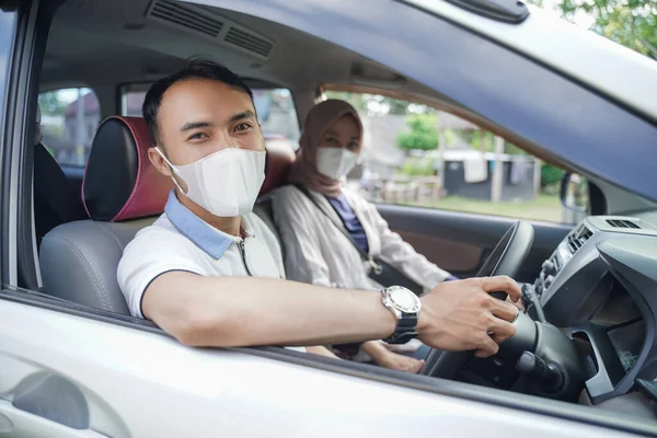 A young asian man in a mask looks at the camera while driving in a car with his partner — Stock Photo, Image