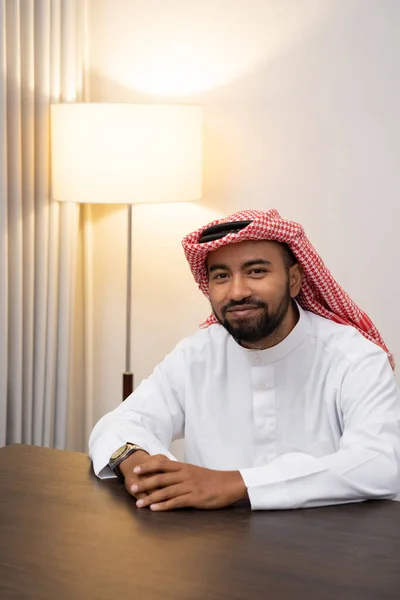 Arabisk man i turban ler mot kameran medan han sitter med båda händerna på skrivbordet — Stockfoto