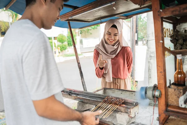 Musulmana mujer ordenar pollo satay de pequeño carrito de comida vendedor. — Foto de Stock