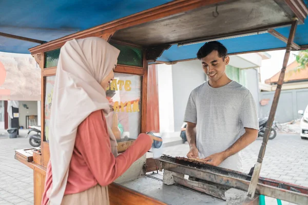 Mulher muçulmana ordenando satay frango de pequeno vendedor de carrinho de comida. — Fotografia de Stock