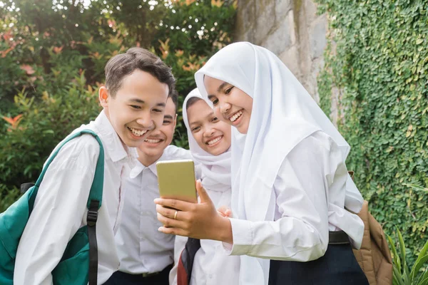 Quattro adolescenti in uniforme delle scuole medie che usano e guardano i cellulari — Foto Stock