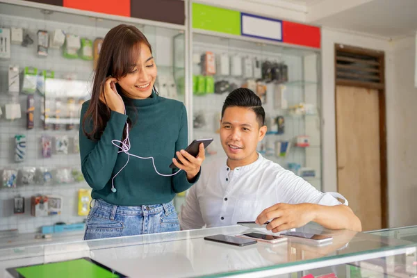 Krásná žena používající sluchátka a mobilní telefon vedle prodavače — Stock fotografie