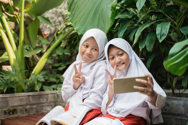 Två barn bär slöja i skolan uniformer använda en smartphone selfie tillsammans medan lärande — Stockfoto