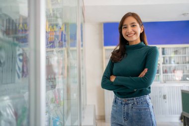 beautiful asian woman smiling with crossed hands near cell phone accessories display case clipart