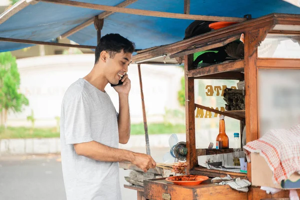 Sate ayam prodejce vaření jídlo, zatímco mluví po telefonu — Stock fotografie