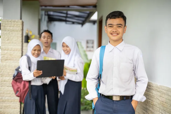 Um asiático adolescente sorri para a câmera no um escola uniforme carregando um escola saco com copyspace — Fotografia de Stock