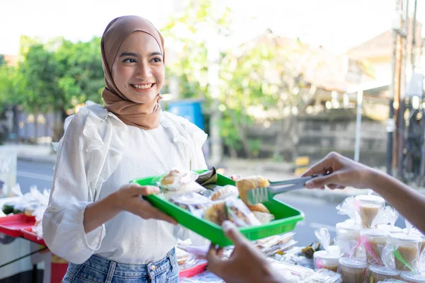 Una hermosa chica en un velo dar una bandeja de plástico de comida takjil — Foto de Stock