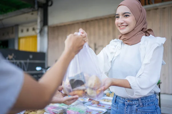 Seorang gadis asia berkerudung memberikan perintah makanan takjil dalam kantong plastik kepada pembeli — Stok Foto