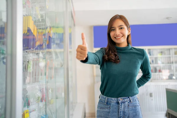 Mooie aziatische vrouw glimlachen met duimen omhoog in de buurt van mobiele telefoon accessoires vitrine — Stockfoto