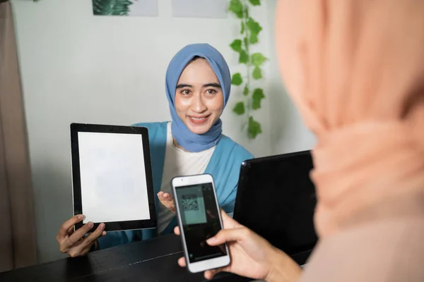 En hijab affärskvinna håller en tablett och visar skärmen för kunder som använder mobiltelefoner samtidigt som de betalar icke-kontanter genom att skanna streckkoder — Stockfoto