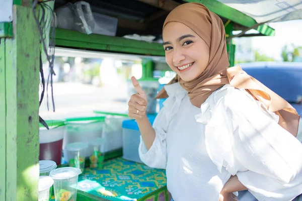 Uma menina bonita em um véu vendendo frutas sorri feliz com um polegar para cima — Fotografia de Stock