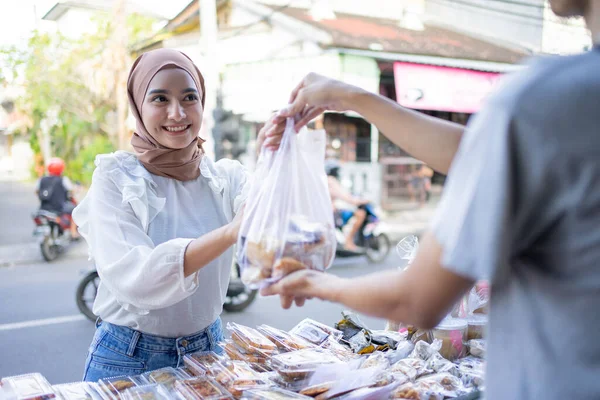 Egy gyönyörű lány fejkendőben vesz egy Takjil ételrendelést egy műanyag zacskóval. — Stock Fotó