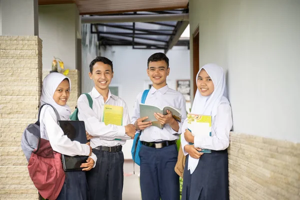 Vier tieners in kleuterschool uniformen stonden in de rij terwijl ze boeken en een laptop droegen — Stockfoto