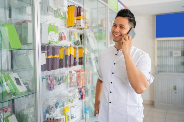 Beau jeune homme passer un appel avec un smartphone dans un magasin de téléphonie mobile — Photo