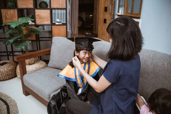 Азійська мати з дитиною готуються до свого доброго випускного дня вдома. — стокове фото