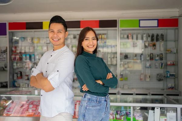 Een knappe jonge man en een mooie jonge vrouw met gekruiste handen staan op een smartphone winkel — Stockfoto